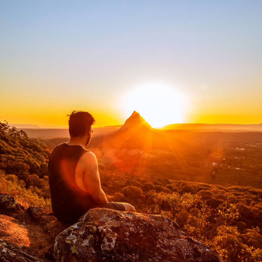 Morning Meditation Benefits -a man sitting on a rock looking at the sunset